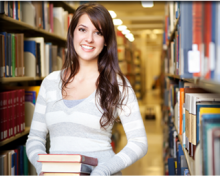 Una joven sonríe y carga varios libros en una biblioteca
